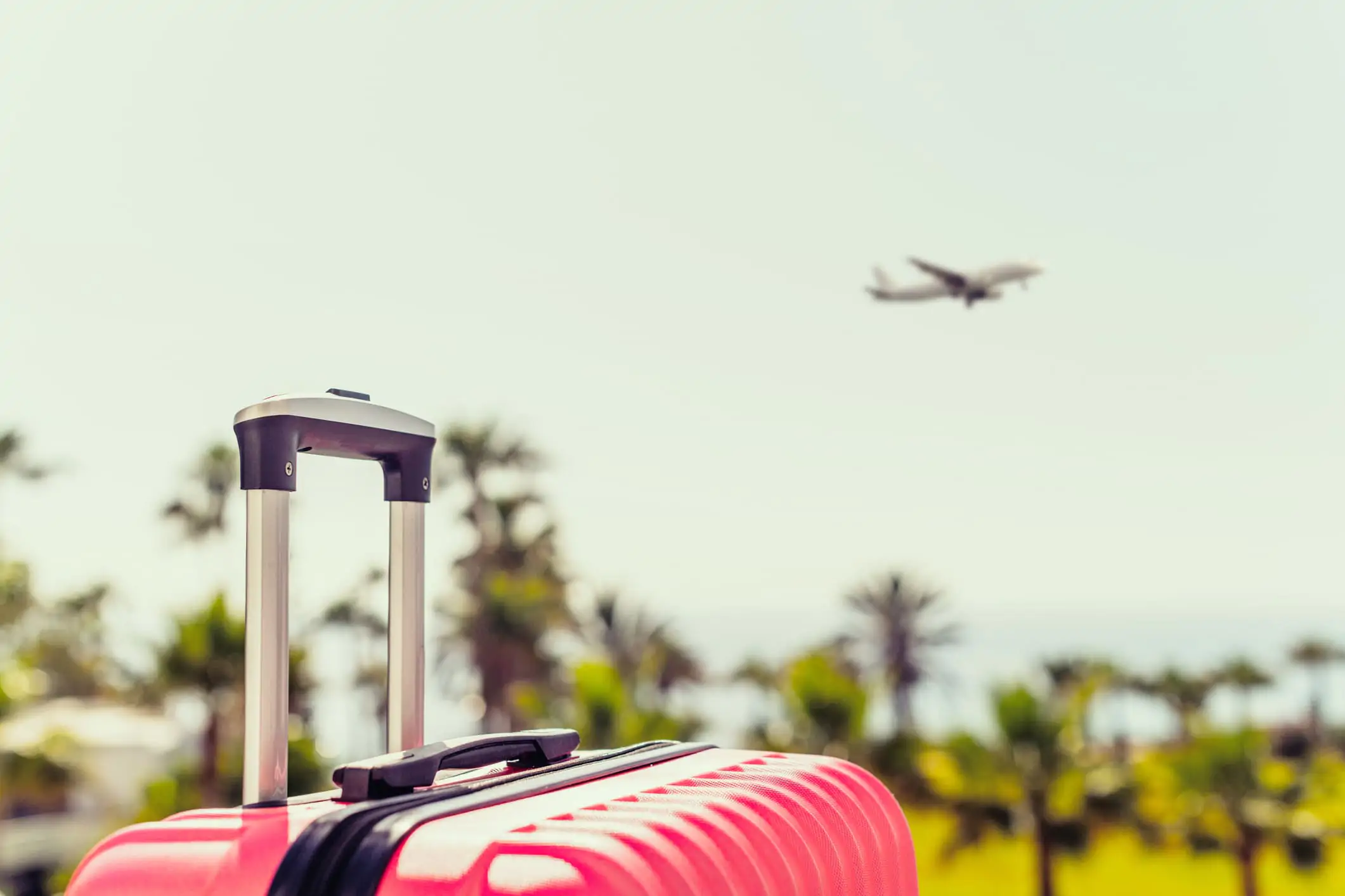 an image of a pink passenger suitcase near a airport while a plane flying over