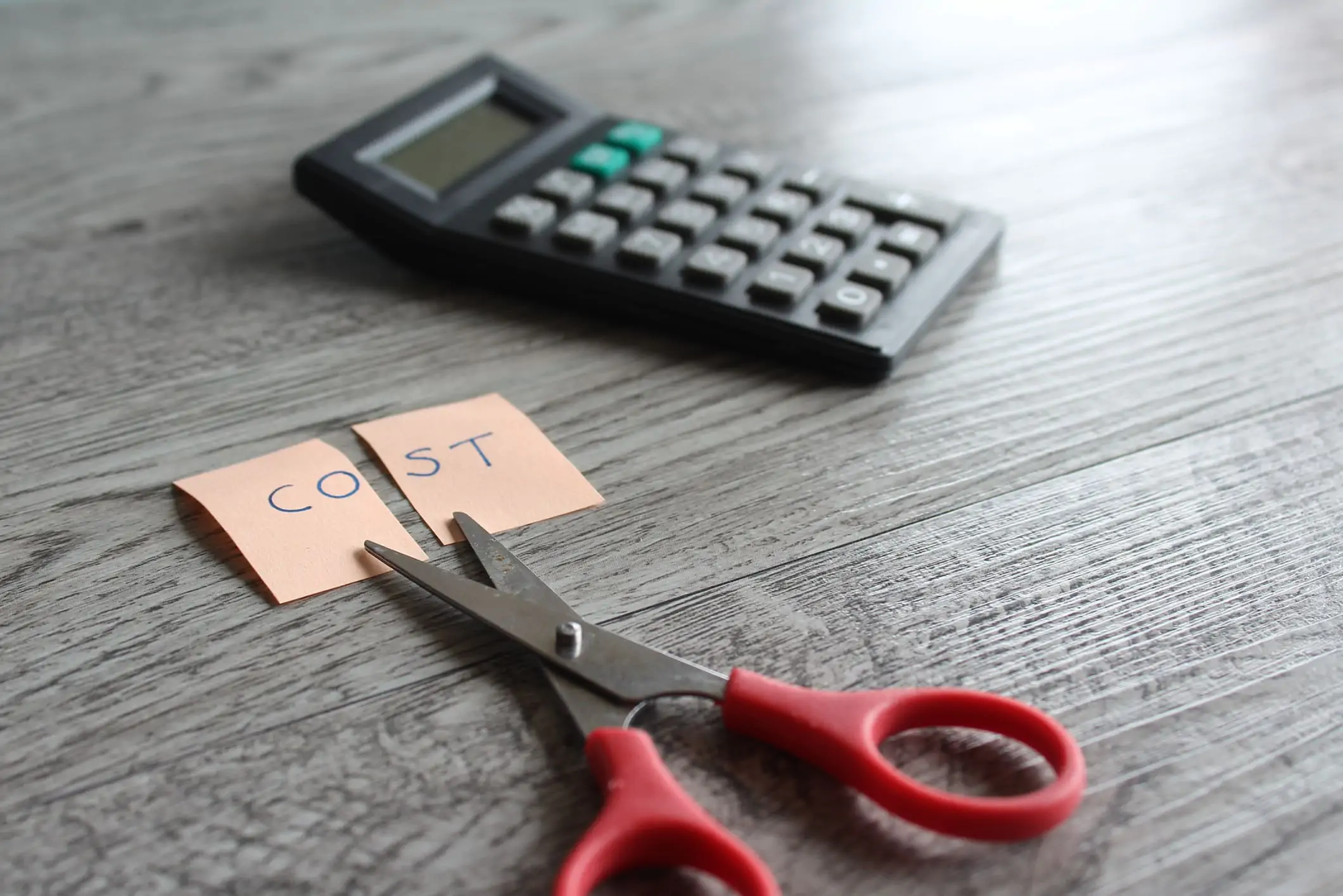 an image of a scissors near a sticky not with "cost" written on it and a calculator