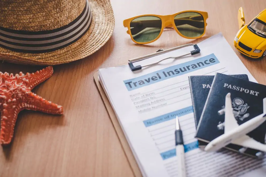 an image of travel insurance documents near some pasports, shades, a hat, a toy starfish and a plane.